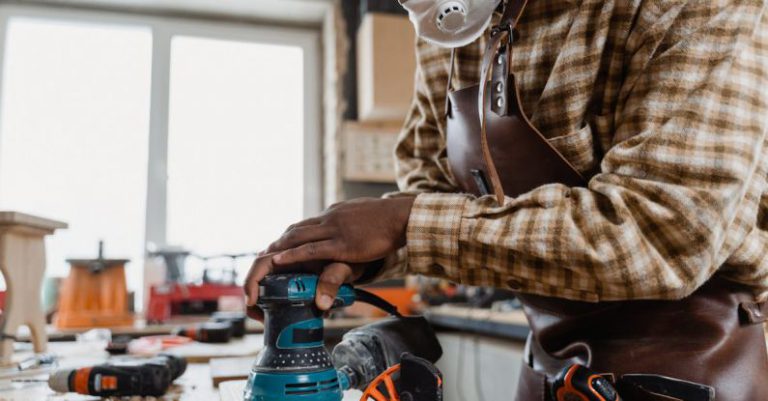 Power Sander - A Man in Checkered Long Sleeves Sanding a Wooden Board