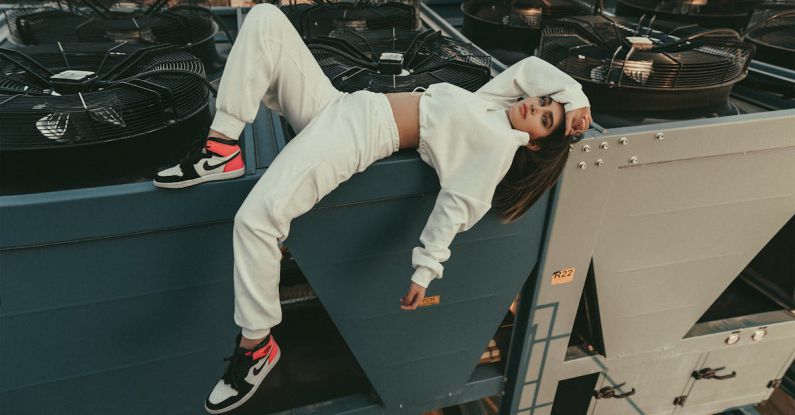 Air Compressor - Full body of stylish female with long hair looking at camera while lying with bent leg on edge of compressor air conditioner on roof