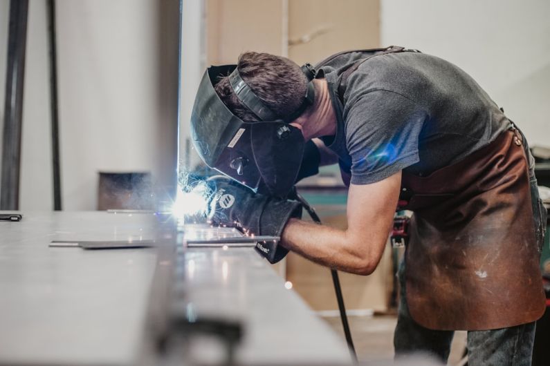 Welder - man in blue t-shirt and brown shorts wearing black helmet