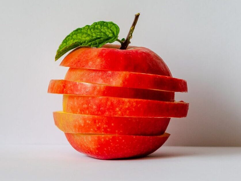 Artistic stack of sliced apple pieces with a fresh green leaf.